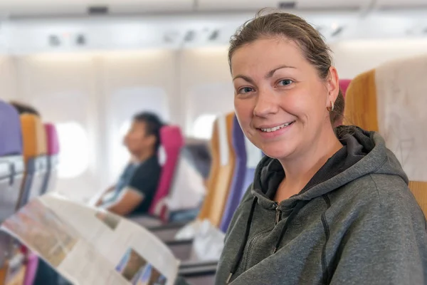 happy airplane passenger with magazine in chair smiling during f