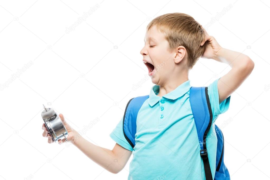 tired yawning schoolboy with an alarm clock on white background