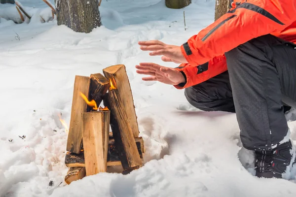 Ein Lagerfeuer im Winterwald und ein Tourist, der sich die Hände wärmt. — Stockfoto