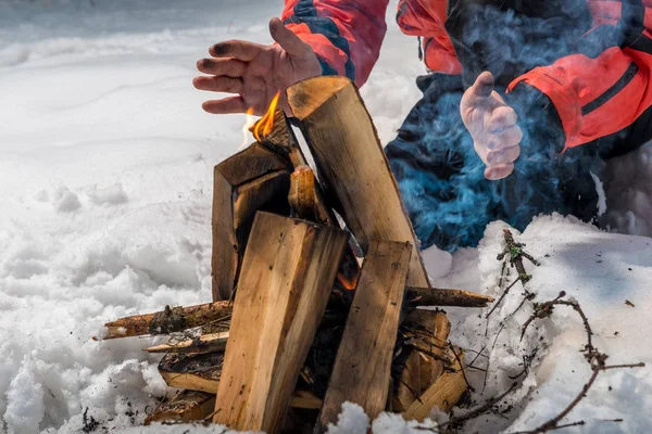 El turista construye un fuego en el bosque de invierno y calienta su han —  Fotos de Stock