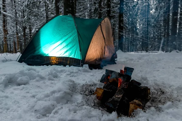 Ein Lagerfeuer im Schnee vor dem Hintergrund eines grünen Zeltes in einem — Stockfoto