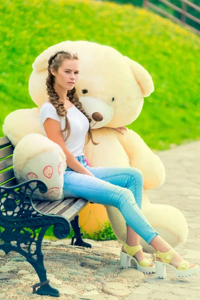 Young beautiful girl in the park with her huge teddy bear on the — Stock Photo, Image