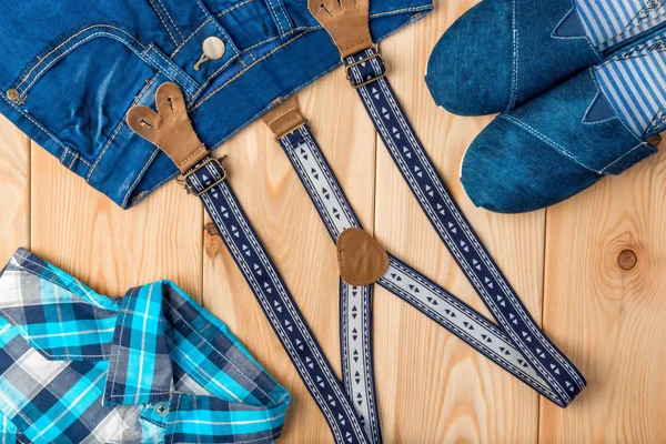 Check shirt, jeans, shoes and suspenders on a wooden background — Stock Photo, Image