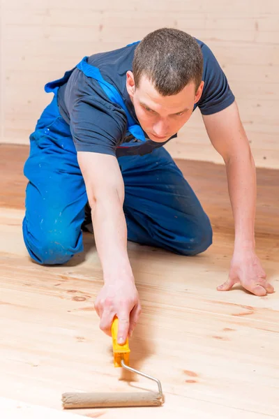 Geschoolde jonge arbeider verfroller op een houten vloer in het huis — Stockfoto