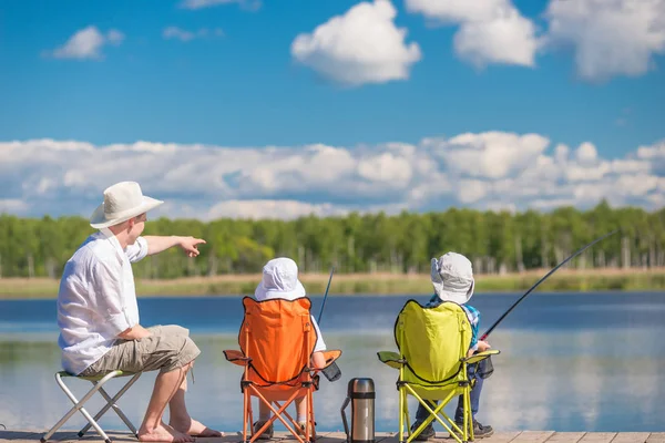 Мужчина с сыновьями сидят на кастрюле и рыбачат — стоковое фото