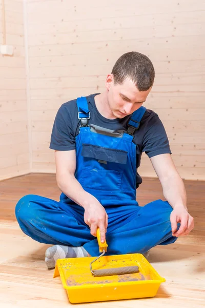 Een man in overalls verf de vloer in een houten huis — Stockfoto