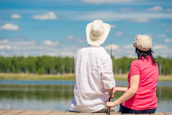 Family couple with a fishing rod sitting on a wooden pier near t — Stock Photo, Image