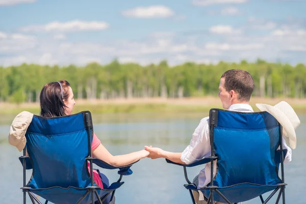 Man and woman are sitting on chairs at the pier near the lake an — Stock Photo, Image