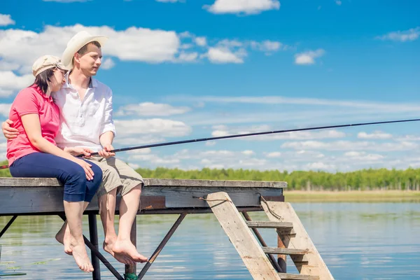 Joven feliz pareja en un muelle de pesca en un hermoso lago — Foto de Stock