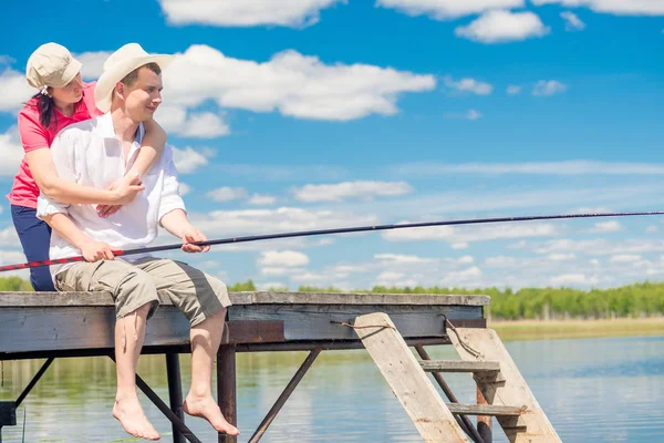 En un muelle de madera, una pareja amorosa con una caña de pescar está pescando — Foto de Stock