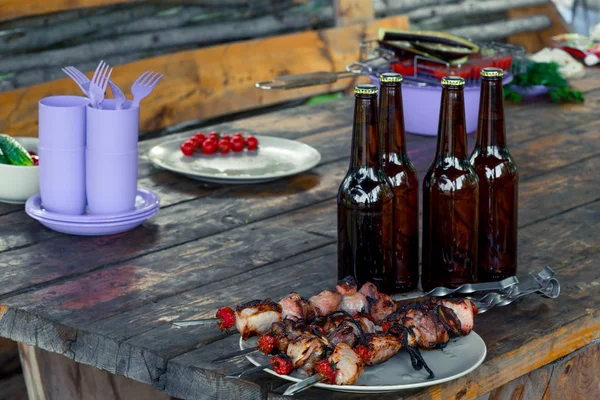 Tasty shish kebab on a plate and a bottle of beer stand on a woo — Stock Photo, Image