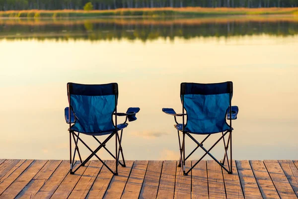 A pair of empty chairs stand on a wooden pier near the lake at d — Stock Photo, Image
