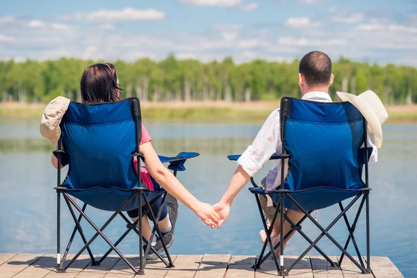 Pár sedí na židlích, na molu v blízkosti jezera a hospodářství h — Stock fotografie