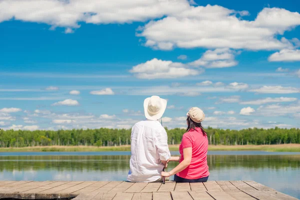Young couple with a fishing rod sitting on a wooden pier near th — Stock Photo, Image