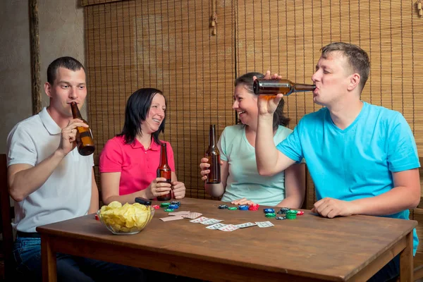 Uma companhia de amigos bebendo cerveja e jogando cartas sentados em — Fotografia de Stock