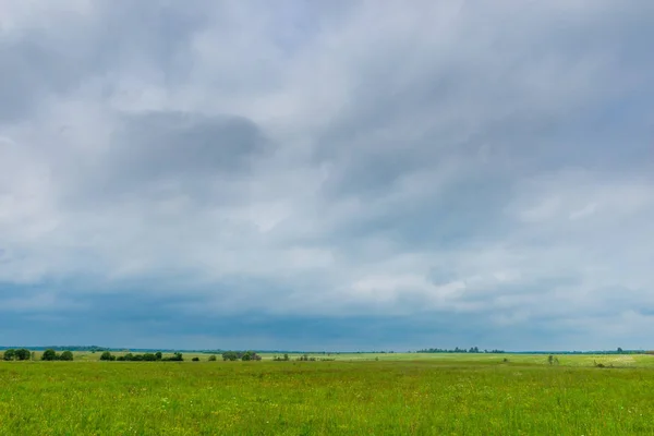 Nubes oscuras y lluviosas cuelgan en un campo de primavera verde en el campo —  Fotos de Stock