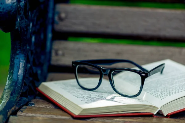 Offenes Buch und schwarze stylische Brille auf einer Holzbank im Par — Stockfoto