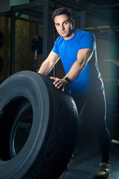 Giovane atleta forte posa con una ruota pesante in palestra — Foto Stock