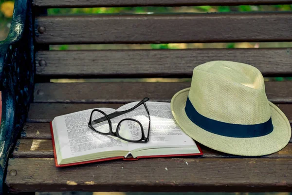 Um livro de romance esquecido, óculos elegantes e um chapéu de palha estão em um — Fotografia de Stock