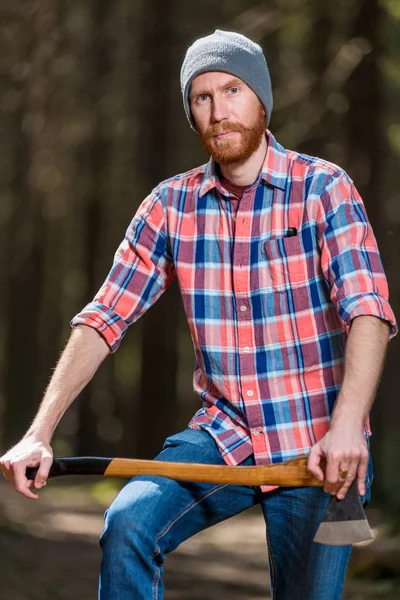 Retrato de um homem em uma camisa xadrez com um machado na floresta — Fotografia de Stock