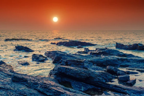 Bright orange sun over the sea and rocky shore. Tinted. — Stock Photo, Image