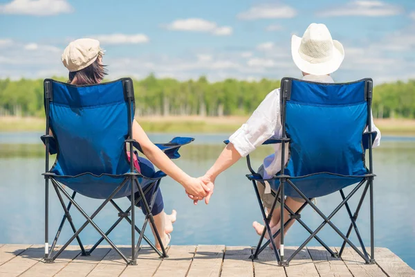 Couple in love sitting on chairs at pier near lake and holding h — Stock Photo, Image