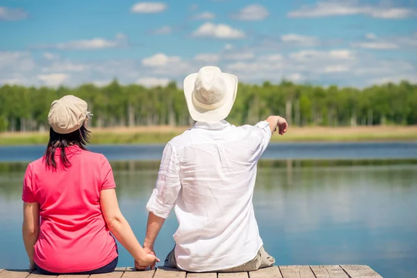 Guy and girl look at the lake sitting on the pier, view from the — Stock Photo, Image