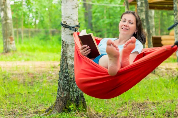Feliz mujer de 30 años leyendo un libro, sentada en una hamaca roja — Foto de Stock