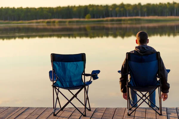 Man in the chair sits near the lake at dawn and enjoys the beaut — Stock Photo, Image