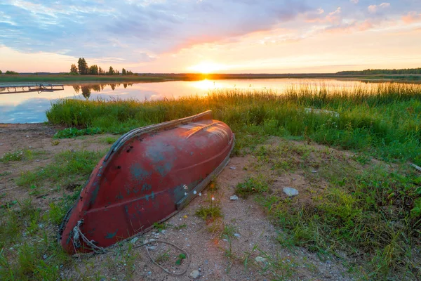 Beeld omgekeerd oude boot aan de oever van het meer bij dageraad — Stockfoto