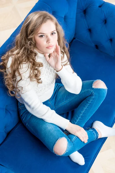 Roztomilá dívka v teplém svetru na gauči v obýváku zobrazení — Stock fotografie