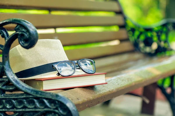Un libro olvidado, un sombrero y gafas se encuentran en el borde de un banco i — Foto de Stock
