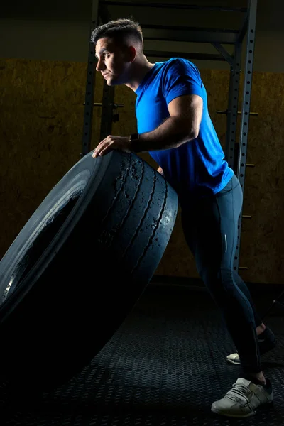 Forte giovane atleta con una grande ruota pesante in palestra — Foto Stock