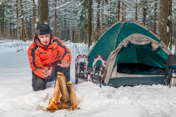 Een bevroren verloren toerist in de buurt van een tent warmt zijn handen door het vuur — Stockfoto