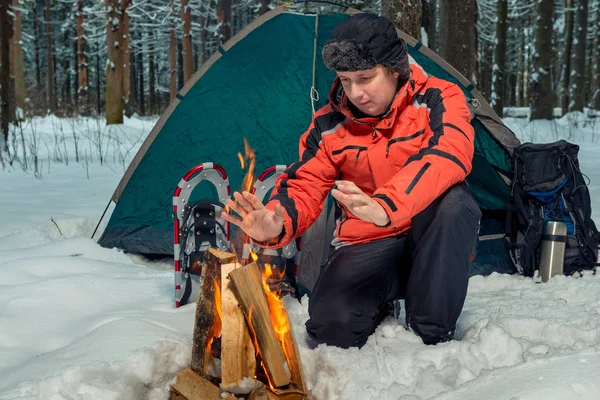 Frozen tourist warms his hands near the fire in a tent camp in t — Stock Photo, Image