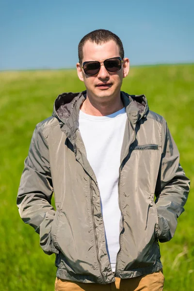 Potret seorang pria dalam jaket dan kacamata hitam di padang rumput hijau — Stok Foto