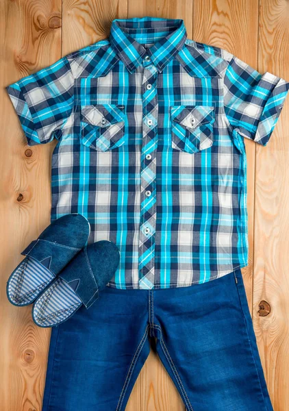 Shoes, checkered blue shirt and jeans for a boy set on a wooden — Stock Photo, Image