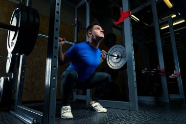 mavi tişört içinde vücut geliştirmeci bir halter salonunda, karanlık ph ile