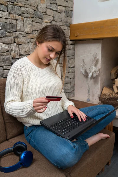 Νεαρή γυναίκα στον καναπέ, κρατώντας πιστωτική κάρτα και να χρησιμοποιούν φορητό υπολογιστή compute — Φωτογραφία Αρχείου