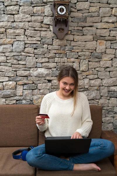 Νεαρή γυναίκα στον καναπέ, κρατώντας πιστωτική κάρτα και να χρησιμοποιούν φορητό υπολογιστή compute — Φωτογραφία Αρχείου