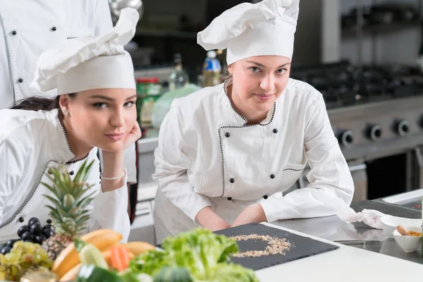 Due giovani cuochi femminili felici che indossano uniformi che lavorano in cucina . — Foto Stock