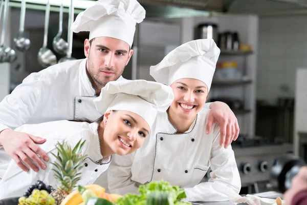 Due donne felici e un maschio giovani cuochi che indossano uniforme di lavoro — Foto Stock