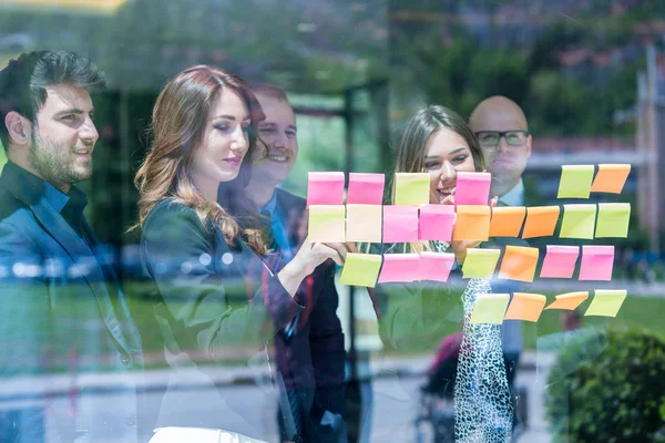 business, startup, planning, management and people concept - happy creative team with stickers on office glass board talking at office