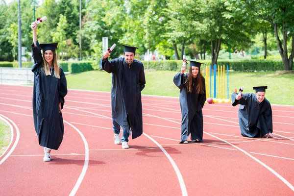 Avläggande av examen grupp studenter firar på athletic spår, prep — Stockfoto