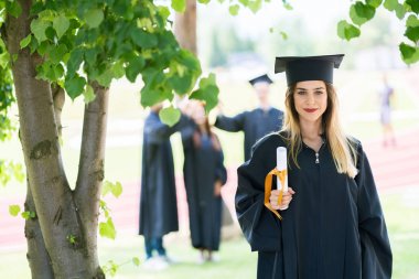Mezuniyet: Öğrenci arkadaşlar arkasında diplomasıyla ile ayakta