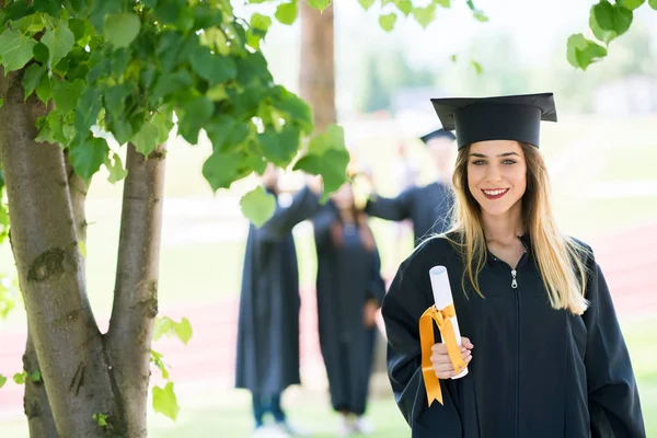 Afstuderen: Student permanent met Diploma met vrienden achter — Stockfoto