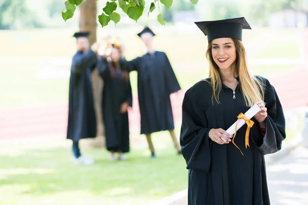 Afstuderen: Student permanent met Diploma met vrienden achter — Stockfoto