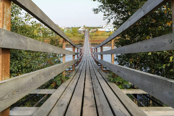 Autumn in the Russian North. Suspension bridge in the village Shikhirikha Arkhangelsk region. Spectacular perspective and symmetry. River Malkurya