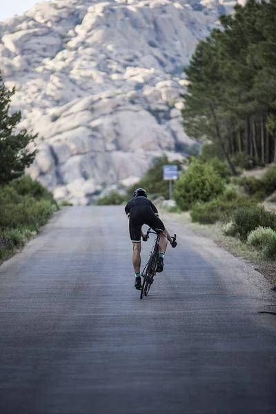 Ciclista subir a la carretera cerca de las montañas rocosas — Foto de Stock