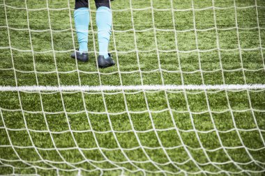 Futbol sahasındaki golü koruyan tanınmamış genç kaleci, kalenin arkasındaki bacakları görüyor